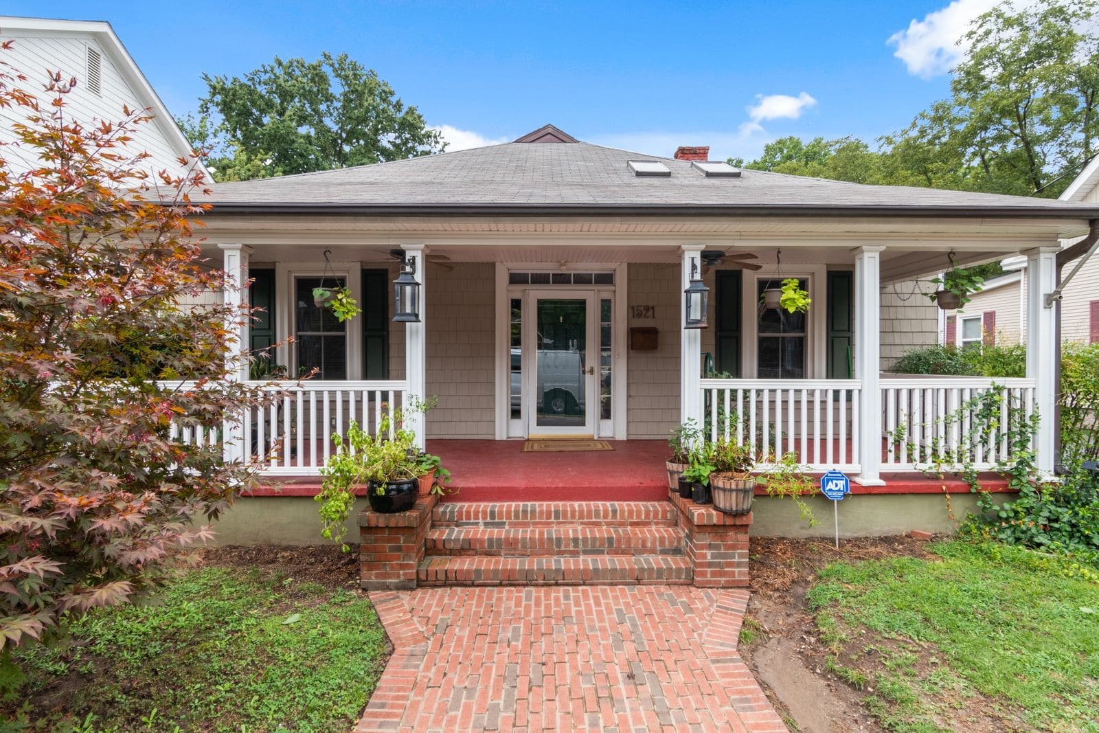Beige ranch home with white columns, red brick walkway, and wraparound porch