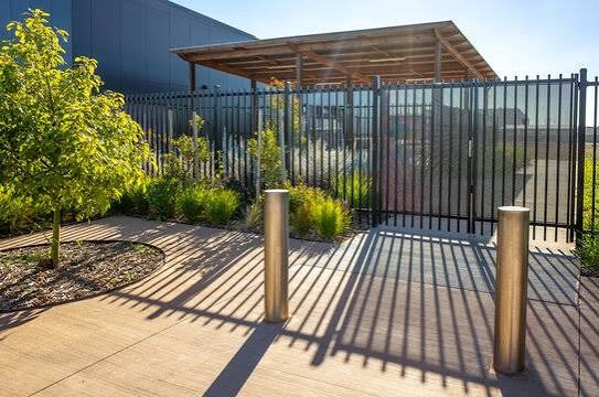 Modern outdoor patio with black metal fence, wooden pergola, concrete pavers, and landscaping
